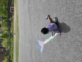 Girls draws on asphalt with colourful chalk