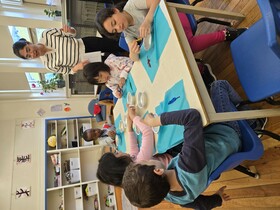 Students engage in hands-on learning at table while teacher watches on