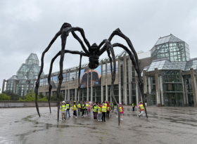 Children in safety vest stand under giant sculpture of spider outside of National Gallery of Canada