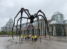 Children in safety vest stand under giant sculpture of spider outside of National Gallery of Canada